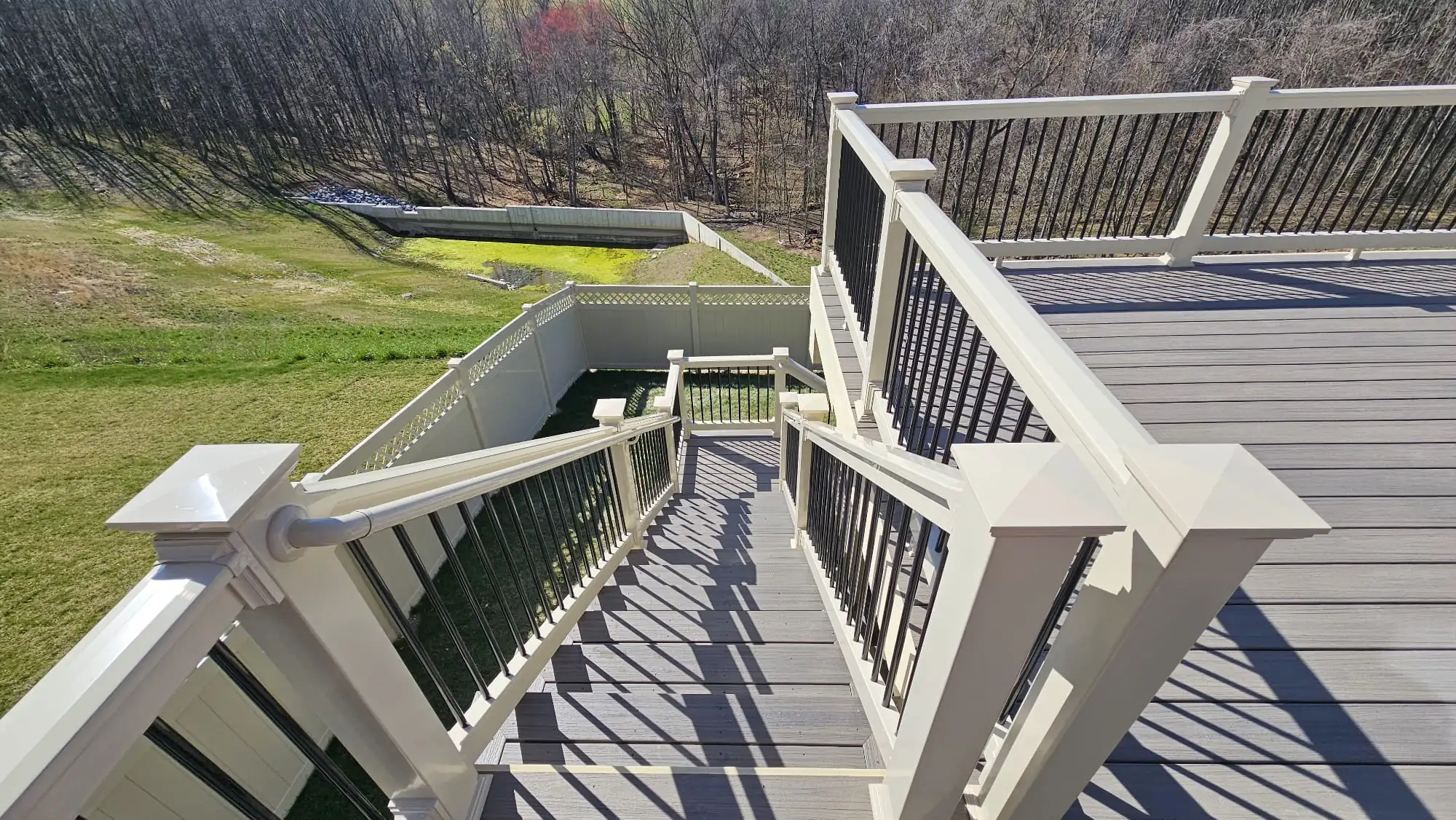 Multi-level composite deck and staircase with white vinyl railings and black metal balusters overlooking a grassy backyard and tree line — Maryland deck railing ideas